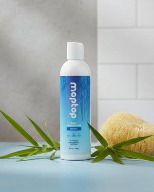 An 8 ounce bottle of Daily Conditioner next to bamboo on a bath