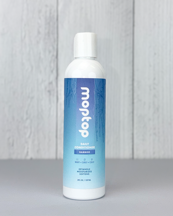 Front view of a Daily Conditioner bottle against white wood