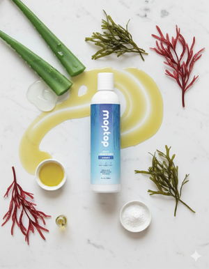 A bottle of Daily Conditioner surrounded by its ingredients, Aloe vera, seaweed, and honey