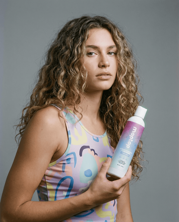 A woman with curly hair hold a Co-Wash Cleansing Conditioner bottle